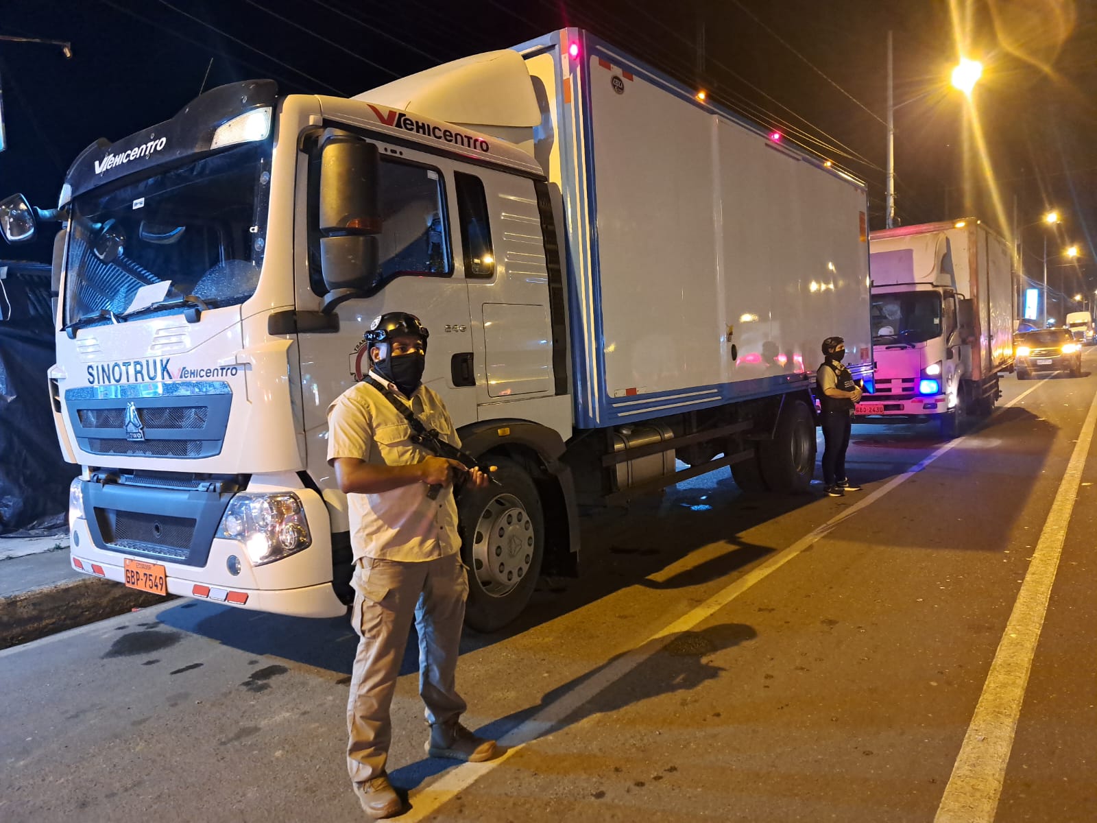 Camión de carga de noche en Guayaquil con un agente armado de First Defense junto a la cabina